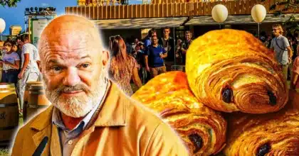Philippe Etchebest souriant lors d’un événement gastronomique, avec en arrière-plan des chocolatines dorées et un public en plein air.