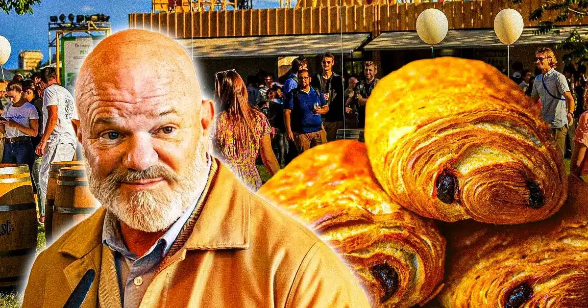 Philippe Etchebest souriant lors d’un événement gastronomique, avec en arrière-plan des chocolatines dorées et un public en plein air.