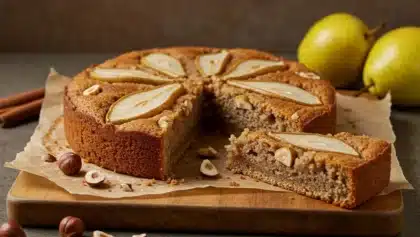 Gâteau moelleux aux poires et noisettes, décoré de tranches de poires sur le dessus et servi sur une planche en bois.