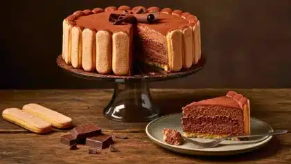 Charlotte au chocolat fondante entourée de biscuits cuillère, décorée de copeaux de chocolat et servie sur un plat noir.