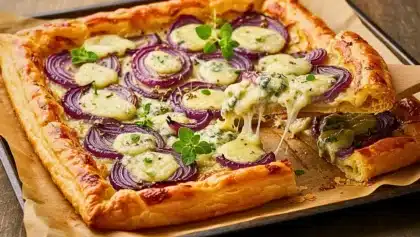 Tarte feuilletée dorée garnie d’oignons rouges et de gorgonzola fondant, servie chaude avec herbes fraîches.