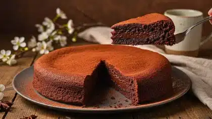 Gâteau fondant au chocolat saupoudré de cacao, avec une part découpée révélant une texture moelleuse et coulante.
