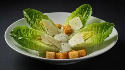 Assiette de salade César avec feuilles de romaine croquantes, copeaux de parmesan, croûtons dorés et sauce crémeuse à la manière de Jean-François Piège.