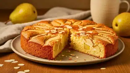 Gâteau moelleux aux poires et aux amandes, doré et fondant, présenté sur une assiette en céramique avec quelques éclats d’amandes.