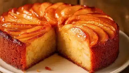 Gâteau aux pommes moelleux et doré, coupé pour révéler une texture fondante, avec tranches de pommes caramélisées sur le dessus.