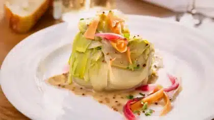 Poireaux fondants nappés de vinaigrette à la moutarde, inspirés de la recette de Paul Bocuse, servis sur une assiette blanche.
