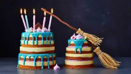 Deux gâteaux à étages décorés de glaçage bleu, de crème violette, de bougies allumées et d’un balai en nougatine posé en diagonale.