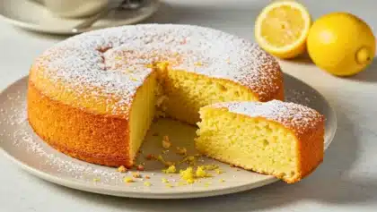 Gâteau moelleux au citron et à la ricotta, saupoudré de sucre glace, avec une part découpée laissant apparaître sa texture légère et fondante.