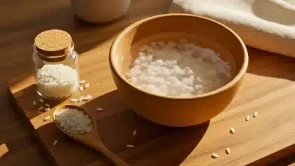 Bol d’eau de riz posé sur une planche en bois, avec une cuillère de riz cru et un petit bocal rempli de grains de riz.