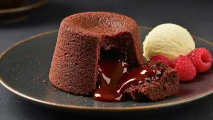 Mi-cuit au chocolat avec cœur coulant, servi avec une boule de glace vanille et des framboises fraîches sur une assiette sombre.
