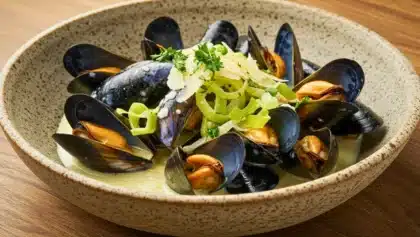 Assiette de moules ouvertes servies avec des poireaux émincés et nappées d’une sauce crémeuse, garnies de persil frais et de copeaux de parmesan.