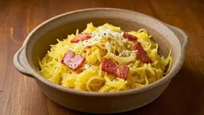 Bol de courge spaghetti filamenteuse mélangée à une sauce crémeuse au parmesan, garnie de lardons grillés et de poivre fraîchement moulu.