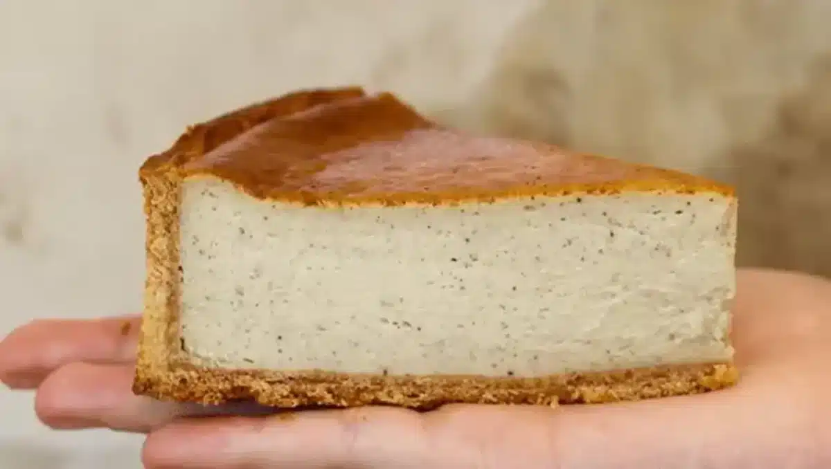 Part de flan à la vanille de la maison Paëma, tenue dans une main, avec pâte dorée et texture fondante marquée de grains de vanille.