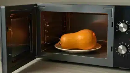 Courge butternut entière posée sur une assiette dans un micro-ondes ouvert, prête à être ramollie pour faciliter l’épluchage.