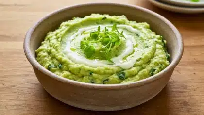 Purée verte de pommes de terre au cresson et fromage de chèvre, servie dans un bol avec un filet de crème et des jeunes pousses.