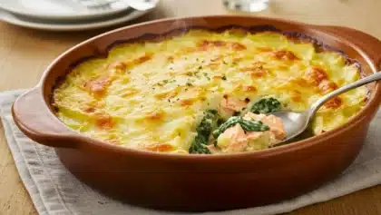 Gratin de saumon, épinards et pommes de terre dans un plat en terre cuite, avec une cuillère révélant l’intérieur crémeux et le dessus doré et gratiné.