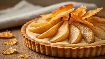 Tarte garnie de poires tranchées et de crème de marrons, décorée de feuilles de pâte filo croustillantes dorées, posée sur un plan de travail en bois.