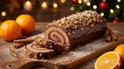 Photographie d'une bûche de Noël au chocolat et streusel, coupée en tranches, sur une planche en bois avec des oranges et des bâtons de cannelle en arrière-plan.