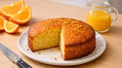 Gâteau moelleux à l’orange coupé en part, sur une assiette, avec des oranges fraîches et du jus d’orange en arrière-plan