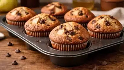Muffins poire et chocolat moelleux dans un moule à muffins, avec des morceaux de poire et des pépites de chocolat visibles