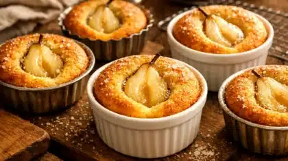 Petits moelleux à la poire faits maison, dorés et moelleux, avec une demi-poire fondante visible, servis dans des ramequins sur une table rustique.