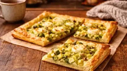 Part de tarte aux poireaux et fromage de chèvre coupée, révélant un intérieur crémeux sur une pâte feuilletée dorée, posée sur une table en bois propre.