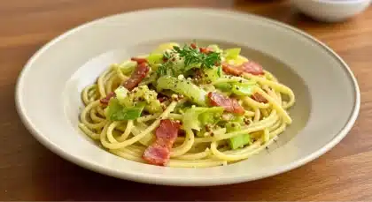 Assiette de pâtes aux poireaux et bacon, garnies d’herbes fraîches.