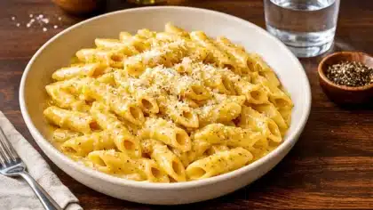 Pâtes penne nappées d’une sauce crémeuse à la moutarde, parsemées de fromage râpé et de poivre noir, servies dans une assiette blanche