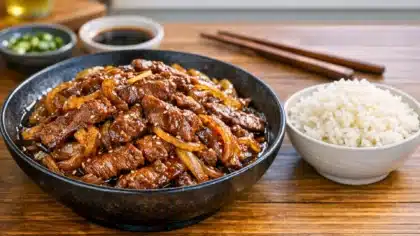 Bœuf aux oignons caramélisés au wok servi avec du riz blanc dans un bol, sauce soja brillante et graines de sésame.