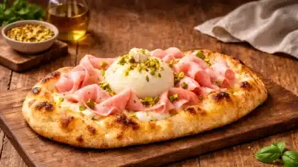 Pinsa romaine garnie de mortadelle, burrata crémeuse et pistaches concassées, présentée sur une table en bois dans une ambiance trattoria chaleureuse.