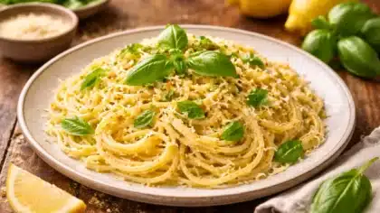Assiette de spaghetti crémeux au citron garnis de basilic frais et de parmesan râpé, servis sur une table rustique.