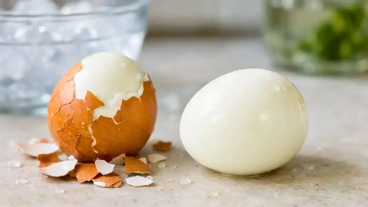 Deux œufs durs sur un plan de cuisine, dont un parfaitement écalé et lisse, à côté d’un autre encore partiellement dans sa coquille.