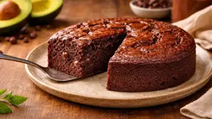 Un gâteau au chocolat très moelleux coupé en part, révélant une texture fondante avec des pépites de chocolat, posé sur une assiette avec des avocats en arrière-plan.
