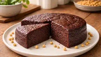Part de gâteau au chocolat fondant sans farine, à base de pois chiches, avec mie dense et humide visible, entourée de quelques pois chiches entiers sur une assiette claire.